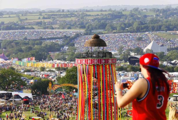 Blick über das Glastonbury Festival mit Menschenmassen, Zelten und einer bunten Aussichtsplattform.