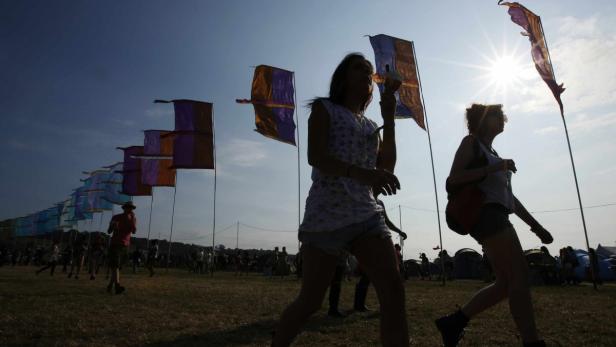 Menschen besuchen ein Festivalgelände mit bunten Fahnen im Gegenlicht.