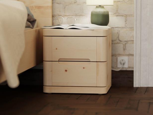 Ein Nachttisch aus hellem Holz mit zwei Schubladen steht neben einem Bett.