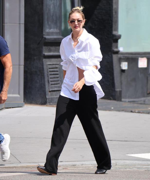 Gigi Hadid geht in einem weißen Hemd und einer schwarzen Hose die Straße entlang.