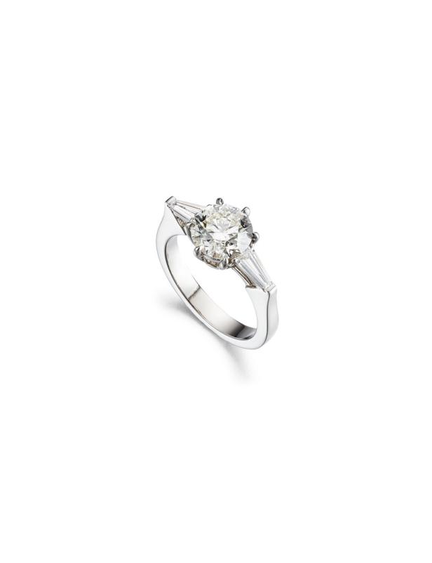 Ein silberner Ring mit einem großen, runden Diamanten und zwei kleineren, baguetteförmigen Diamanten.
