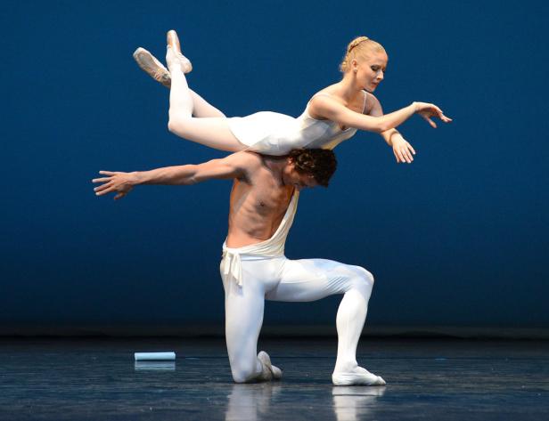 Ein männlicher Tänzer kniet, während eine Ballerina auf seinen Schultern in einer Hebefigur balanciert.