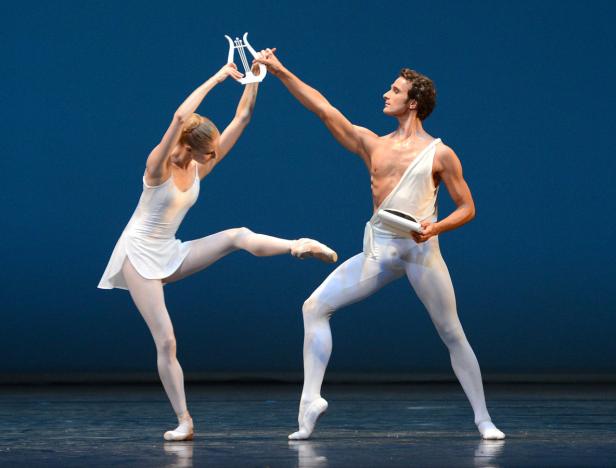 Zwei Balletttänzer in weißen Kostümen führen eine Szene mit einer Harfe auf.