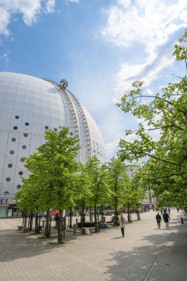 Der Ericsson Globe in Stockholm, teilweise von Bäumen verdeckt, an einem sonnigen Tag.