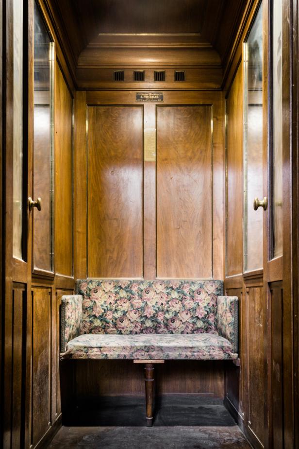 Ein altmodischer Aufzug mit Holzwänden und einer Sitzbank mit Blumenmuster.