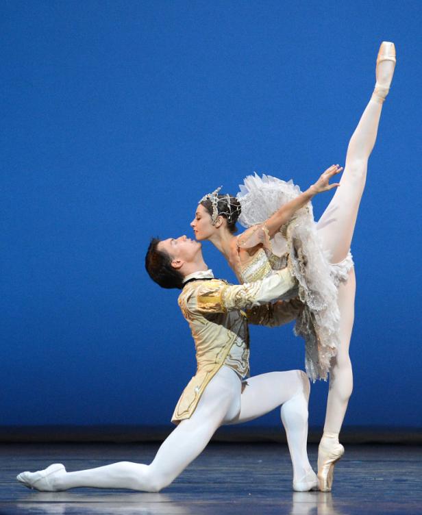 Ein Ballettpaar tanzt vor einem blauen Hintergrund, die Ballerina auf einem Bein in der Luft.