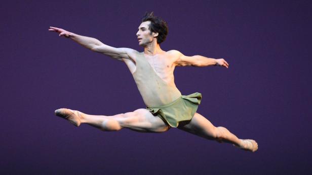Ein männlicher Balletttänzer springt in einem Kostüm vor einem violetten Hintergrund.