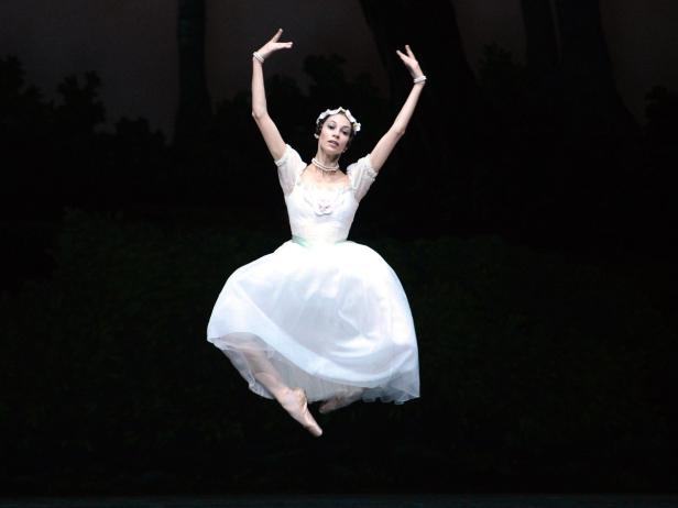Eine Ballerina in einem weißen Tutu springt auf einer Bühne.