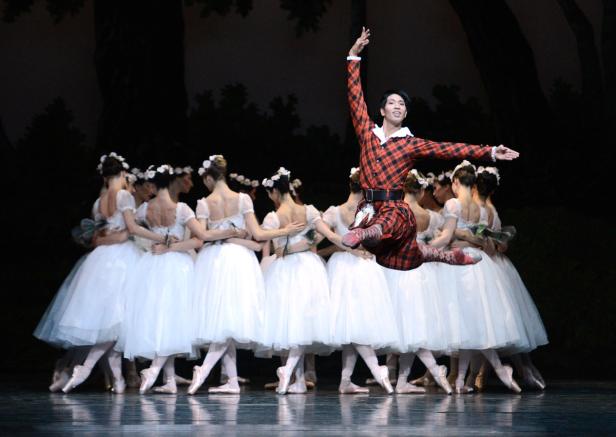 Ein Tänzer in karierter Kleidung springt vor einer Gruppe Ballerinen auf der Bühne.