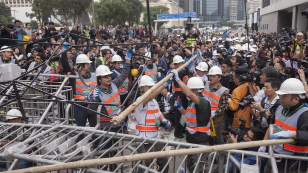 Eine Menschenmenge, einige mit Helmen und Warnwesten, steht hinter einer Barrikade.