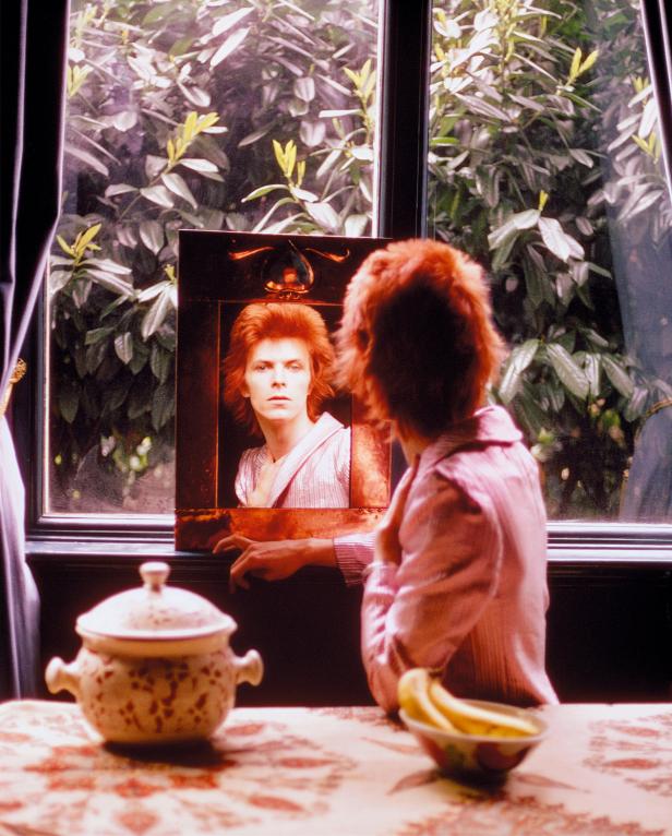 David Bowie betrachtet sein Spiegelbild vor einem Fenster.