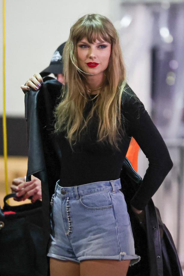 Taylor Swift trägt eine schwarze Bluse und Jeansshorts.