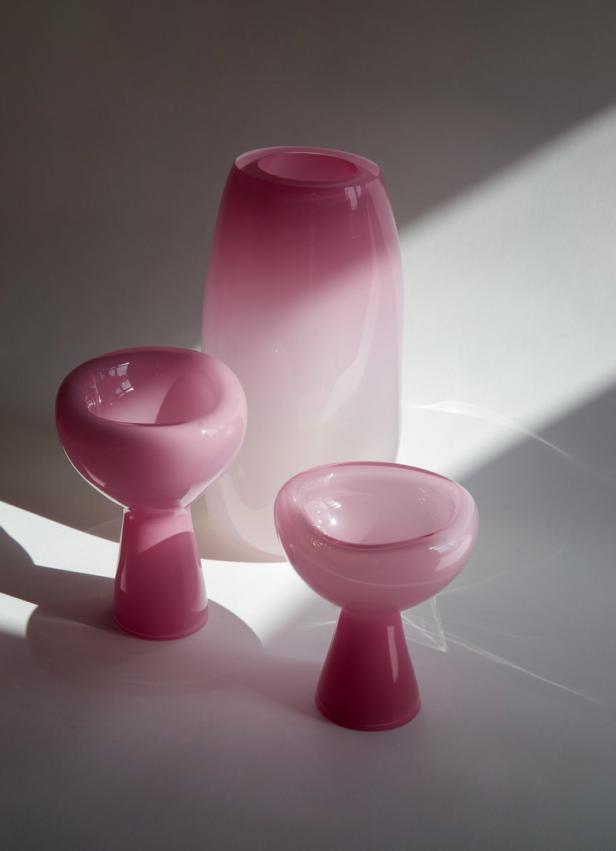 Zwei rosa Kelche und eine Vase aus Glas stehen auf einem Tisch.