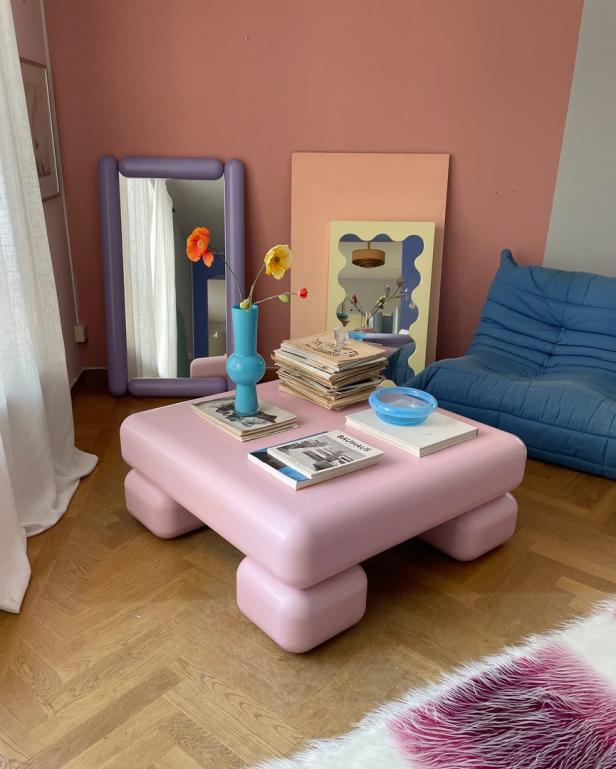 Ein rosa Couchtisch mit Büchern und Blumen steht in einem farbenfrohen Wohnzimmer.