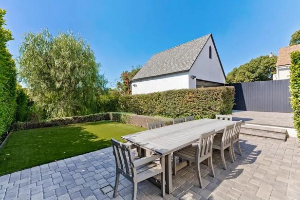 Ein Gartentisch mit Stühlen steht auf einer gepflasterten Terrasse neben einem Rasen.