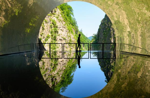 Eine Person steht in einem Tunnel und blickt auf eine Schlucht.