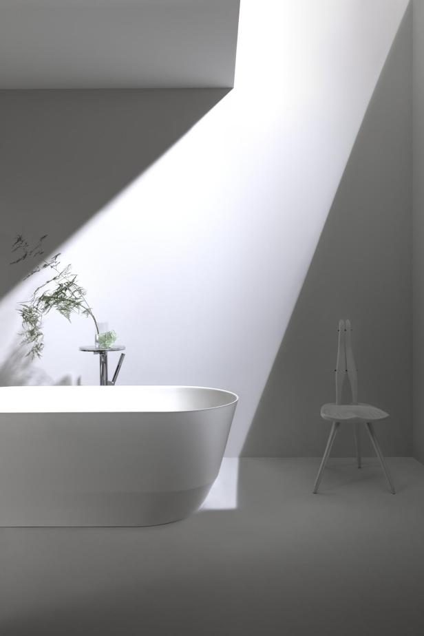 Ein minimalistisches Badezimmer mit Badewanne, Stuhl und Pflanzen, beleuchtet durch einen Lichtstrahl.