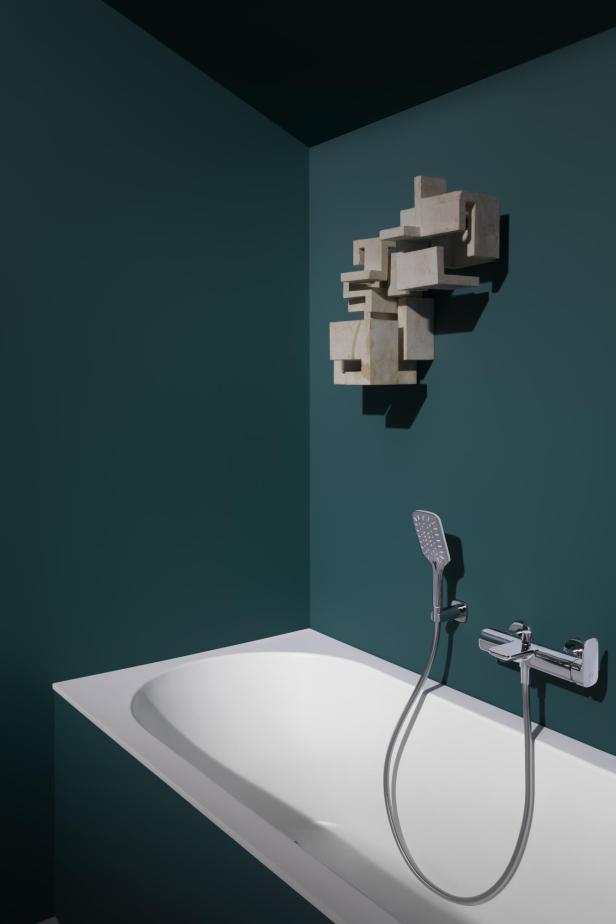 Ein Badezimmer mit einer weißen Badewanne, einer modernen Armatur und einer abstrakten Skulptur an der Wand.