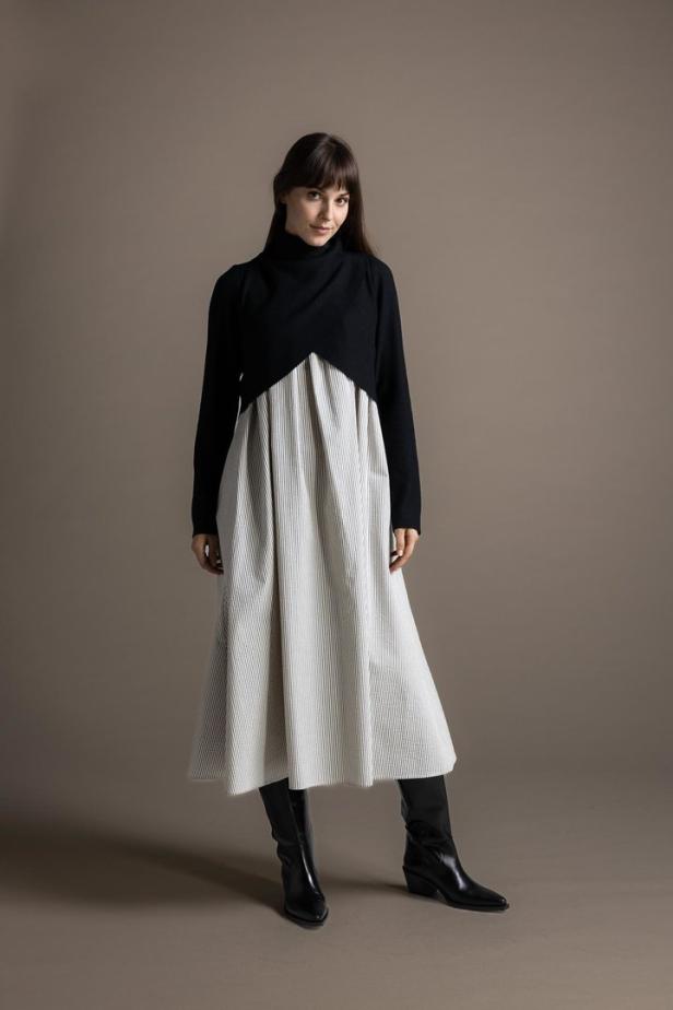 Eine Frau mit langen Haaren trägt ein schwarz-weißes Kleid und schwarze Stiefel.