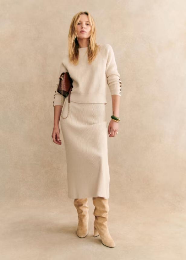 Eine Frau in einem beigen Strickrock und Pullover mit brauner Handtasche von Sézane.