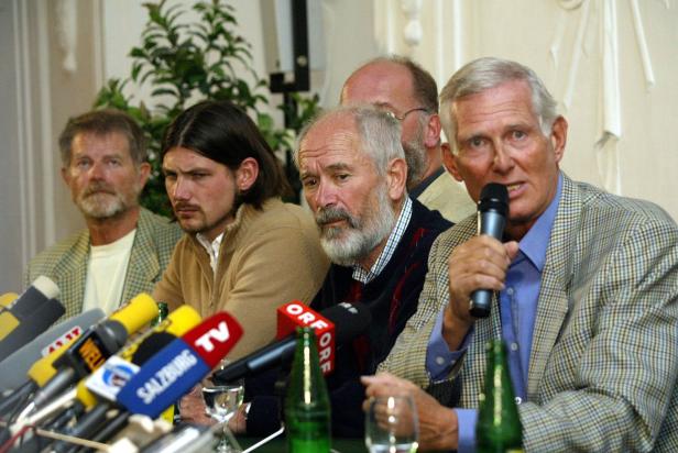 Mehrere Männer sitzen an einem Tisch mit Mikrofonen bei einer Pressekonferenz.