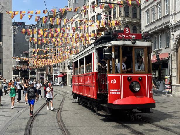 Eine rote Straßenbahn fährt durch eine belebte Straße in Istanbul, geschmückt mit bunten Flaggen.