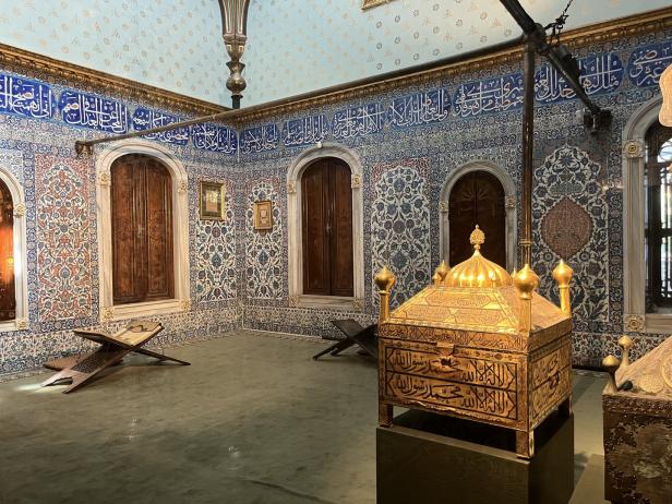 Ein reich verzierter Raum mit türkisfarbenen Wänden, blauen Fliesen und einer goldenen Truhe.