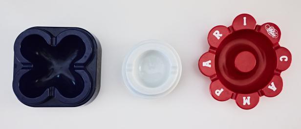 Drei Aschenbecher in Blau, Weiß und Rot liegen nebeneinander auf einem weißen Hintergrund.