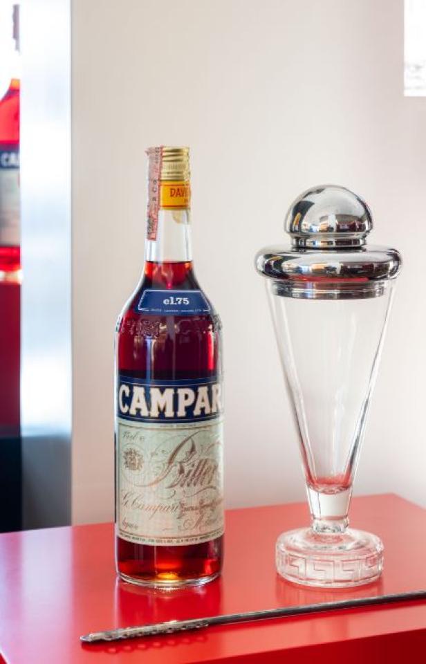 Eine Flasche Campari und ein Cocktailglas auf einem roten Tisch.