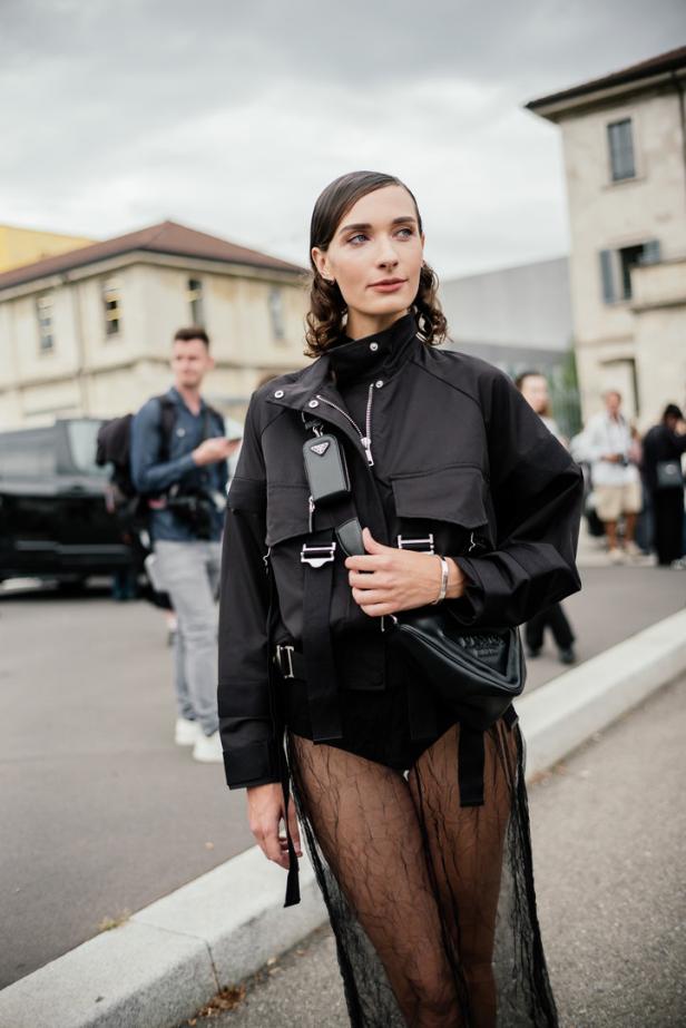 Eine Frau mit dunkler Jacke und transparentem Rock posiert auf der Straße.