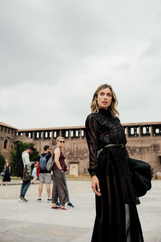 Eine Frau in einem schwarzen Kleid posiert vor dem Castello Sforzesco in Mailand.