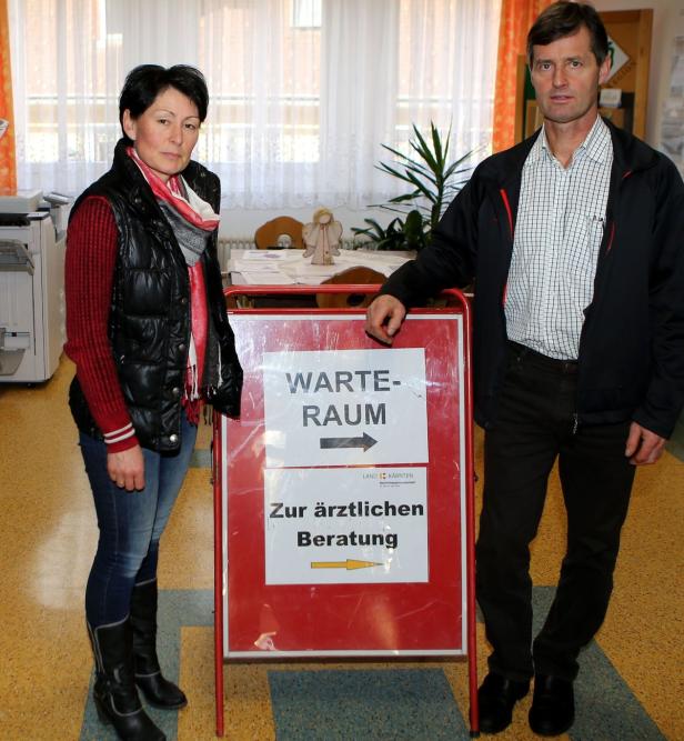 Zwei Personen stehen neben einem Schild, das auf den Warteraum und die ärztliche Beratung hinweist.