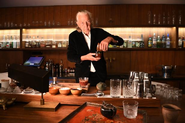 Ein Barkeeper mixt einen Drink hinter einer Bar mit Spirituosenregalen.