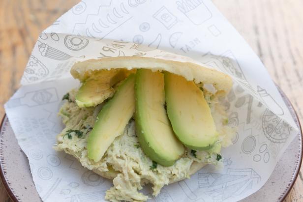 Eine Arepa gefüllt mit Hühnchensalat und Avocadoscheiben.