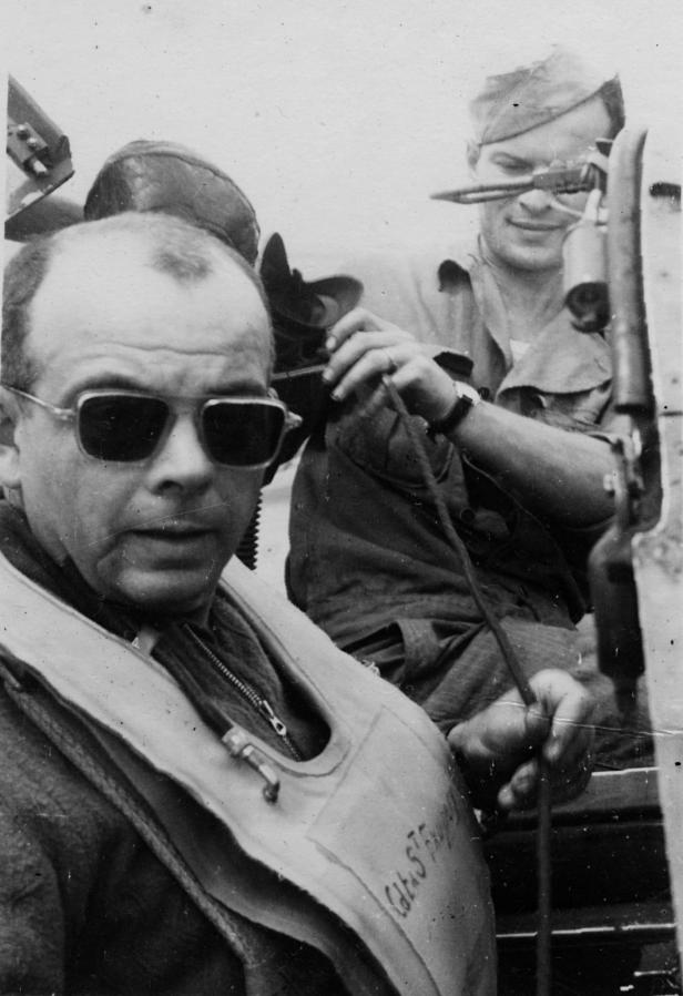 Zwei Männer in Flugausrüstung, der vordere mit Sonnenbrille und Schwimmweste.