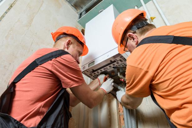 Workers are connecting the pipes to the gas boiler. Workers are connecting the pipes to the gas boiler.