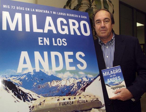 Ein Mann posiert neben einem Poster und einem Buch mit dem Titel „Milagro en los Andes“.