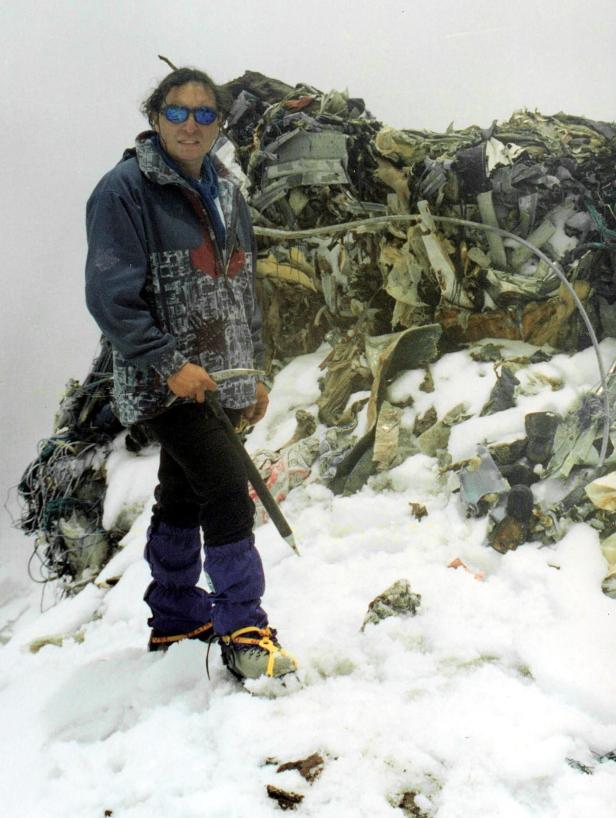 Ein Bergsteiger steht mit einem Eispickel neben einem Haufen Müll im Schnee.