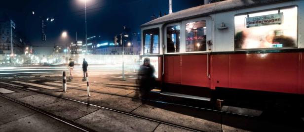 Eine rote und weiße Straßenbahn steht nachts in einer belebten Stadt.