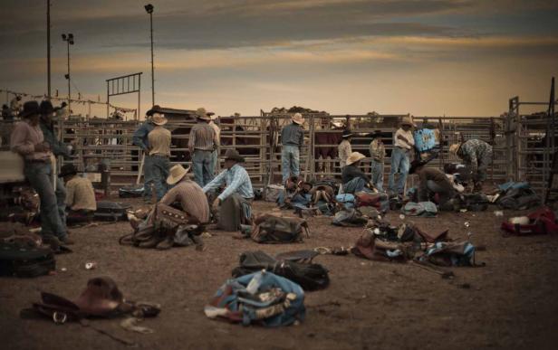Eine Gruppe von Cowboys bereitet sich auf einem staubigen Feld auf ein Rodeo vor.
