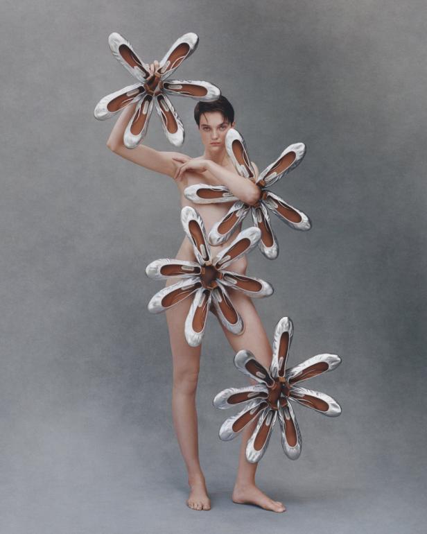 Eine Frau posiert mit silbernen Ballerinas, die wie Blumen um ihren Körper angeordnet sind.