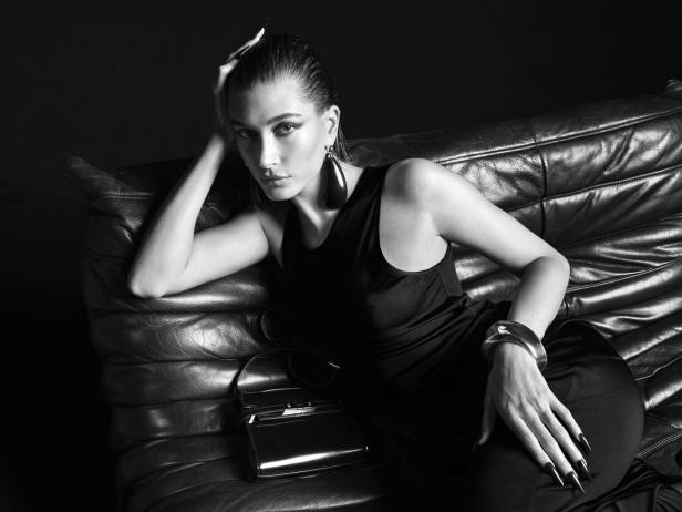 Eine Frau mit dunklem Kleid und auffälligem Schmuck liegt auf einem Ledersofa.