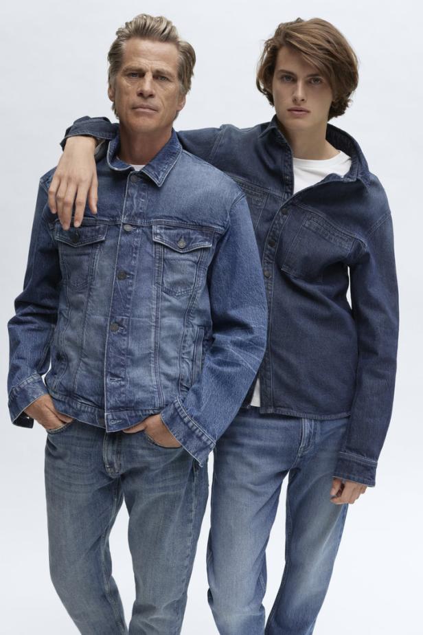 Zwei Männer posieren in Jeansjacken und Jeanshosen vor einem hellen Hintergrund.