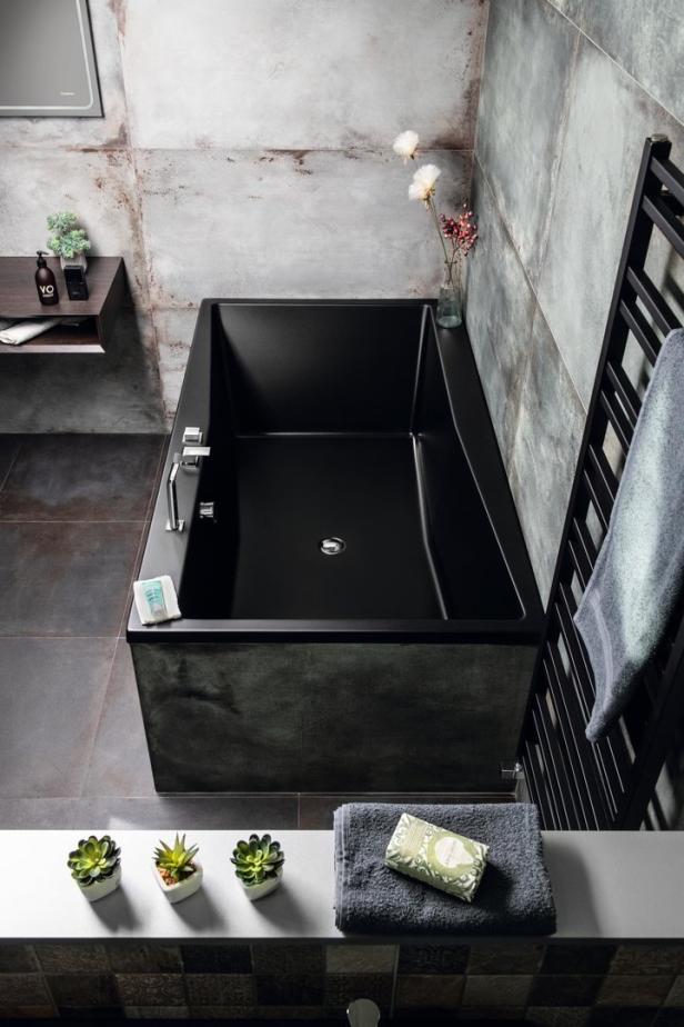 Eine moderne, rechteckige Badewanne in Schwarz steht in einem Badezimmer mit grauen Fliesen.