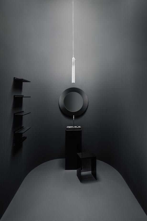 Ein minimalistisches Badezimmer in dunklen Grautönen mit runden Spiegel und Hocker.
