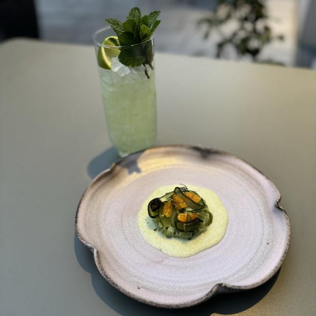 Ein Teller mit einer Vorspeise und ein Cocktail mit Minze stehen auf einem Tisch.