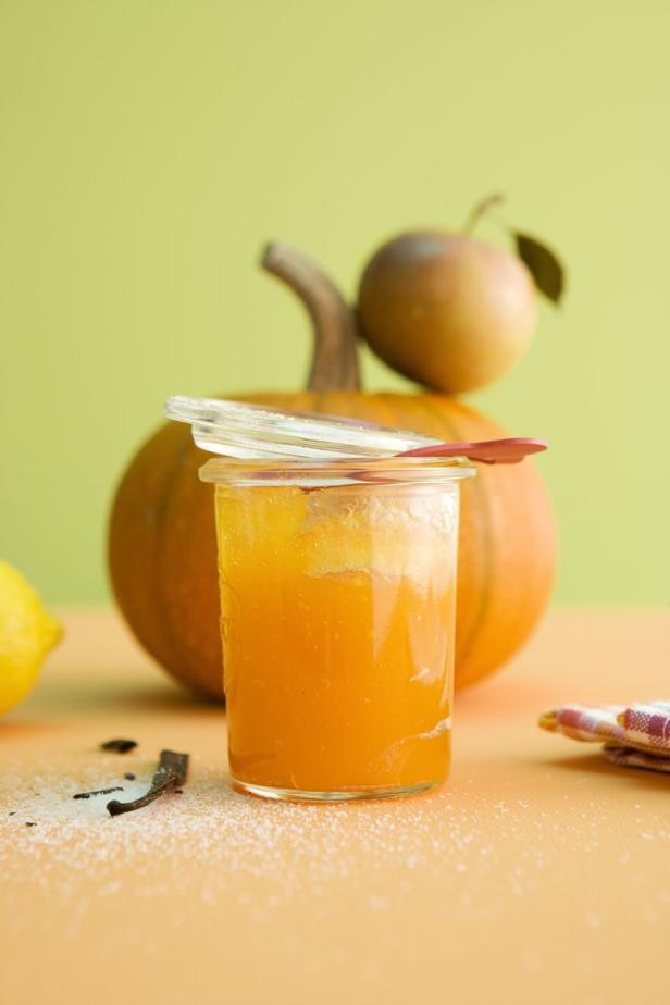 Ein Glas Kürbismarmelade steht vor einem Kürbis und einer Birne.