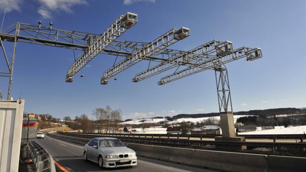Ein silberner BMW fährt unter einer Mautbrücke auf einer Autobahn hindurch.