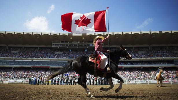 Eine Reiterin mit Cowboyhut und Kanada-Flagge auf einem Pferd in der Calgary Stampede Arena.