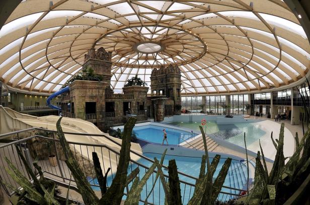 Ein großes Hallenbad mit Wasserrutschen und einem Kuppeldach aus Holz.